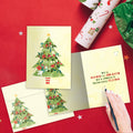 Load image into Gallery viewer, The inside of Tree-Free’s Navidad Tree card, with the cover and envelope in the background.