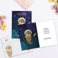 Load image into Gallery viewer, The inside of Tree-Free’s Otter This World card, with the cover and envelope in the background.
